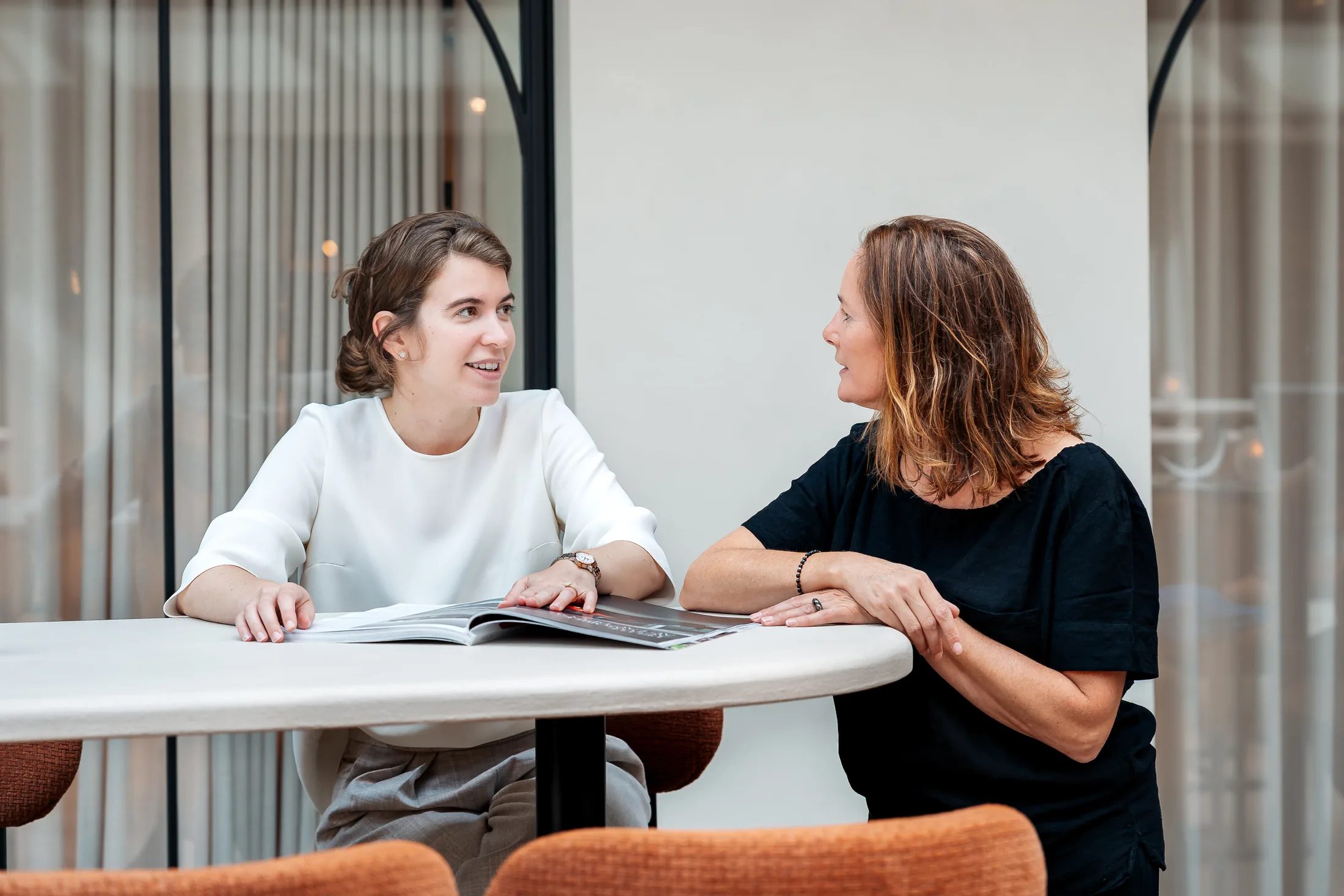 Alexia Hoste en Charlotte Knockaert in gesprek aan een tafel op kantoor, met een dossier voor zich.