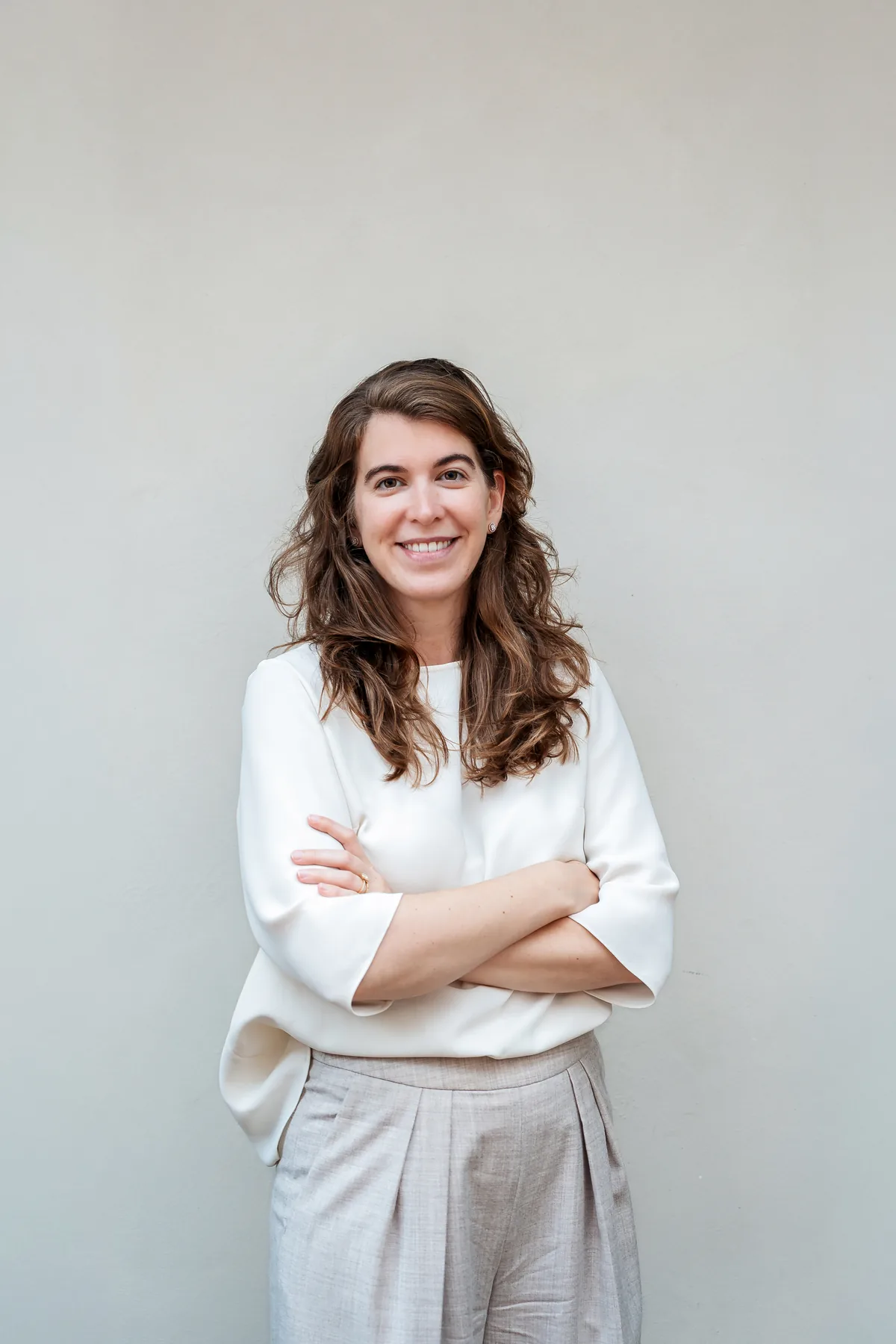 Charlotte Knockaert, met de armen gekruist voor een lichte muur.